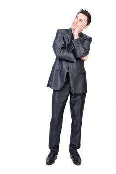 Full length of dreamy young male model with dark hair in elegant suit looking away while standing against white background with hand on cheek