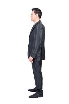 Side view of concentrated young male entrepreneur with dark hair in elegant suit standing against white background and looking away