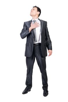 Full length of honest young male in elegant suit and tie putting hand over heart while standing against white background and listening to anthem