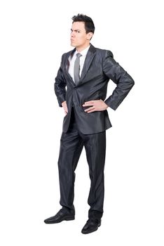 Full body of nervous and irritated male boss standing with hands on waist and looking at camera with frown face in studio against white background
