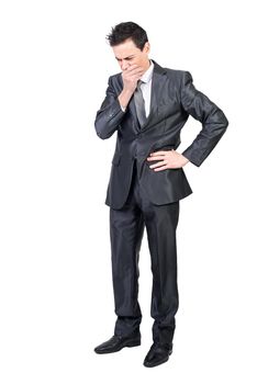 Full body of worried male executive manager wearing formal suit standing with hand on waist and covering mouth while expressing stress in studio against white background