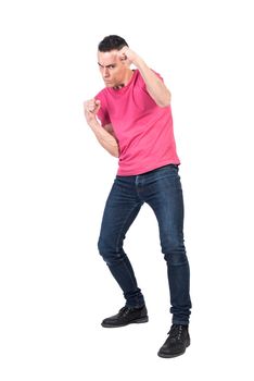 Full body of serious young male fighter in casual outfit looking at camera seriously while standing in boxing stance with clenched fists against white background