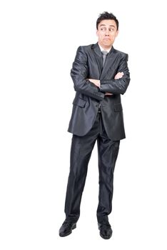 Full body of surprised young male employee with dark hair in elegant suit standing against white background with crossed arms and looking away with doubt