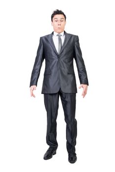 Full length of serious young male manager in formal suit and tie with dark hair looking at camera with astonishment while standing isolated on white background