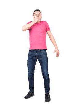 Full body man in casual clothes looking at camera with shock and covering mouth after accidentally telling secret against white background