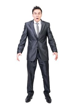 Full length of shocked young male manager in formal suit and tie with dark hair looking at camera with opened mouth while standing in studio against white background