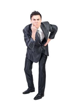 Full body of serious young male manager with dark hair in formal suit pointing at eye and gazing at camera while standing against white background with hand on waist