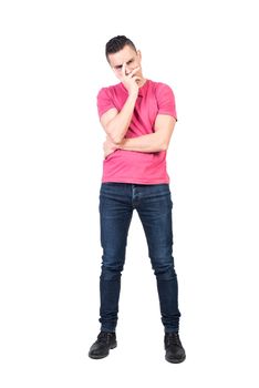 Full length bored male in jeans and pink t shirt covering face with hand and looking at camera with discontent isolated on white background