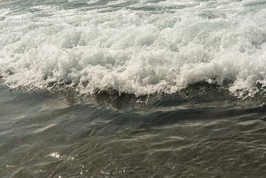 From above black and white of foamy wavy gray ocean water with ripples and splashes on sandy beach in daytime