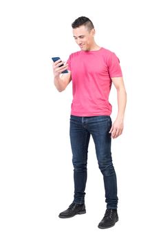 Full body of positive male in casual wear surfing modern cellphone while standing isolated on white background in light studio