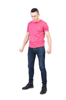 Full body of angry muscular male model with stylish haircut in pink t shirt and jeans clenching fists and looking at camera against white background