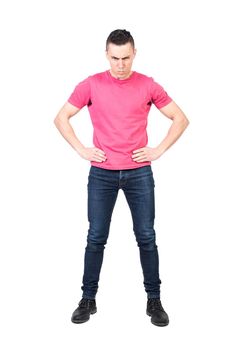 Full length of confident annoyed male model with dark hair in casual outfit looking at camera with serious face expression while standing against white background with hands on waist