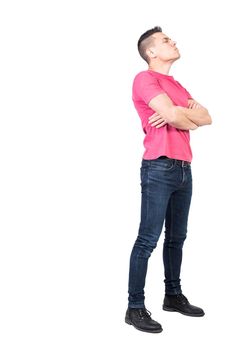 Side view of young offended male with dark hair in casual wear standing isolated on white background with crossed arms