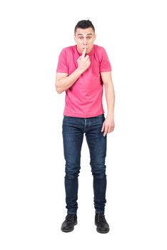 Full length ashamed male in jeans and pink t shirt touching lips and looking at camera while trying to hide his mistake against white background