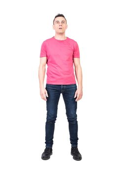 Full length astonished male in jeans and pink t shirt opening mouth and looking at camera in shock isolated on white background