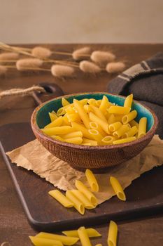 Penne pasta in wooden cutting board on rustic kitchen countertop.