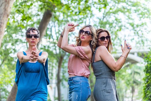 Three mature female friends making a gun gesture with their hands and posing. Middle aged female friends having fun.