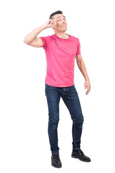 Full body of self assured young male model with dark hair in casual clothes touching forehead and looking at camera against white background