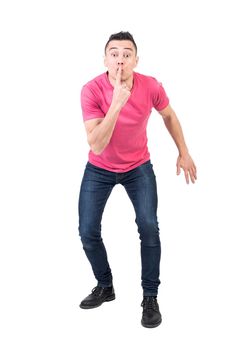 Full body of male model with eyes wide open asking to be quiet with finger on lips on white background