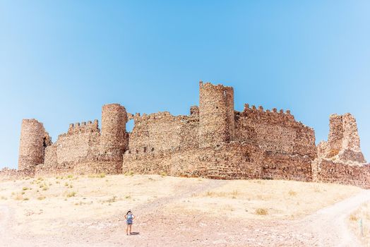 Ancient walled castle on a hill with a woman standing in front of it. Almonacid Castle, Spain.