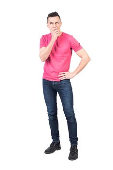 Full body of male model standing with hand on waist and showing expression of hesitation while looking away with thoughtful gaze