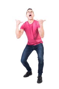 Full body of crazy male model wearing casual outfit yelling loud with opened mouth and showing rock n roll gesture against white background