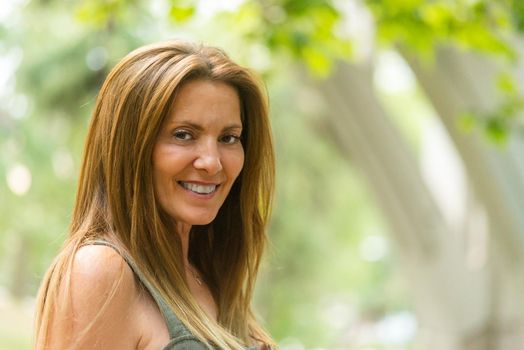Long hair mature woman smiling looking at camera. Portrait of a brown hair adult woman outside.