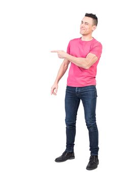 Full body of positive male model in casual clothes pointing aside while standing isolated on white background in light studio