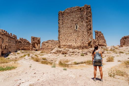 Woman in her back standing in front of a tower of a medieval castle in the sun. Almonacid Castle, in Spain