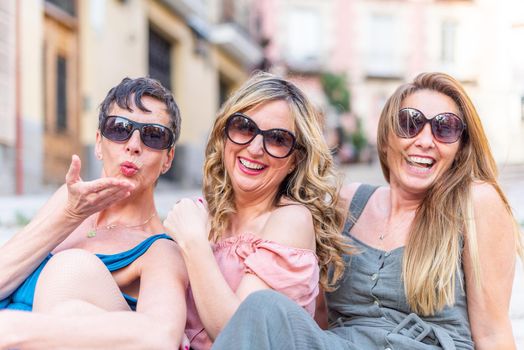 Three cheerful mature female friends with sunglasses laughing and blowing kisses. Middle aged friends sharing time together and having fun.