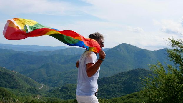 Bisexual, gay, old man, male, transsexual walk with LGBTQIA flag, rainbow peace in pride mounts on the nature on a day and celebrate Bisexuality Day or National Coming Out Day