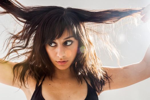 Pretty brunette girl with long hair, looking to the side while disheveled, on white background, close up