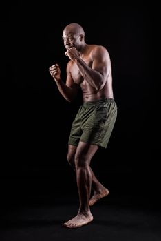 Side view of a muscular adult male standing in defensive boxing pose on a black background. African American man wearing only shorts in a studio.