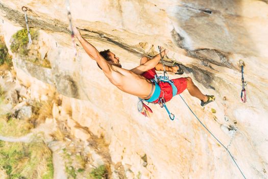 Rock climber holding himself with one arm extended upward on the rock. Climber with bare torso climbing a rock wall.