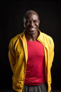 Portrait of an African American man standing looking at the camera and smiling. Adult male in yellow jacket and red t-shirt in a studio with black background.