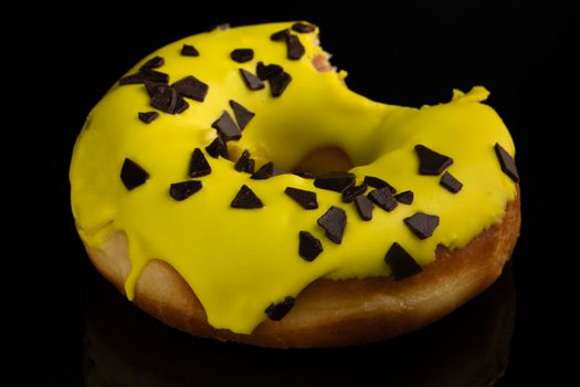 Close up view Delicious bitten chocolate donut on an empty black background. banana donut with yellow frosting. High quality photo