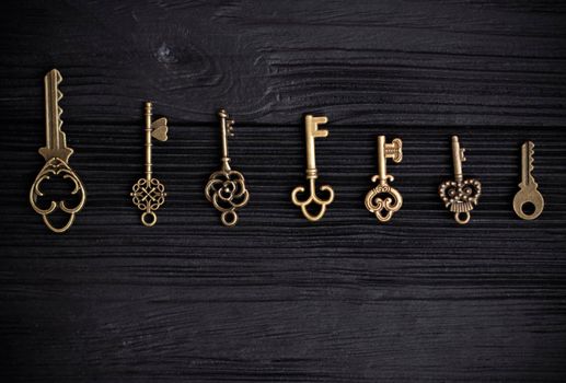 varied, small decorative keys lie in a row on a black wooden background. The concept of the selection of the key to the heart. space for text. High quality photo