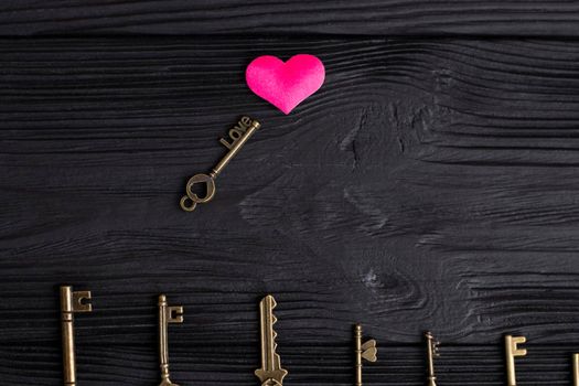 set of antique copper keys. small key with the inscription love, lies on a black wooden background near a pink heart. Heart keys concept, key selection. High quality photo