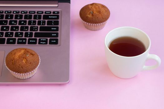 a cup of tea near a laptop. fresh muffins on a pink background. Lifestyle concept in pink, glamorous workplace. High quality photo