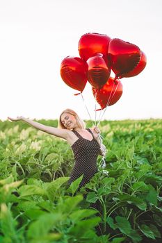 Pretty woman in retro red dress posing with heart-shaped balloons in green field. Birthday, holiday, celebrate freedom concept. High quality photo