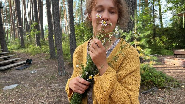 Beautiful woman with curly hair smelling meadow flowers in the woods.