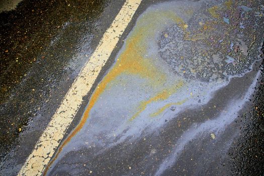 Gasoline spill on asphalt with a white dividing strip in a car park as a texture or background.
