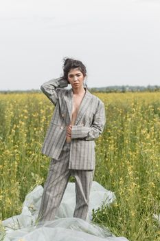 An Asian model poses in a field of yellow flowers for a clothing brand, polyethylene is the main props for a photo shoot. The concept of manufacturing clothing from recycled plastic. A woman in a pantsuit is standing on a plastic bag.