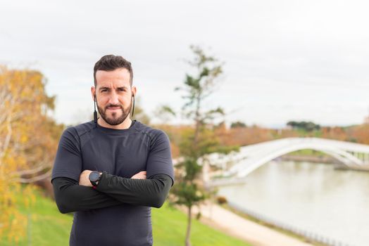 Caucasian sportsman with headphones is standing with crossed arms . High quality photo