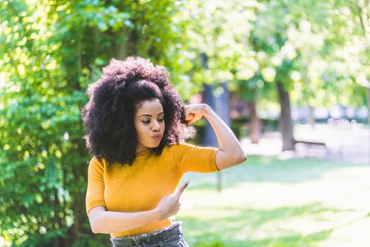 Portrait of pretty afro girl in a garden, pulling out biceps muscle. Selective focus.