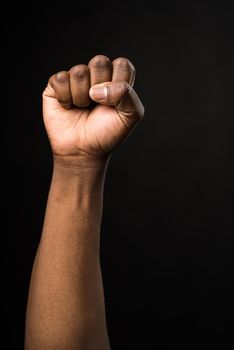 Raised fist of a black man, in a fighting attitude. on black background.