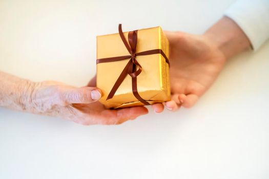 Female hands hold a gift closeup, top view. A young girl gives a nice packed surprise to her mother, grandmother with love, remembers elderly relatives, visits during holidays, takes care of them.