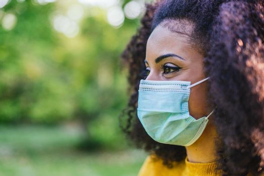 Pretty afro woman smiling with face mask in a garden. Selective focus.