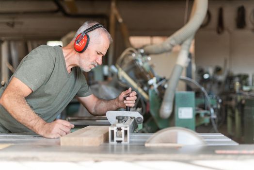 male worker cutting wood with accuracy on a sliding table saw, horizontal full view