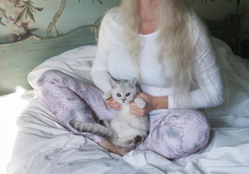 a middle-aged woman with long blond hair meditates in the morning in bed with a kitten,